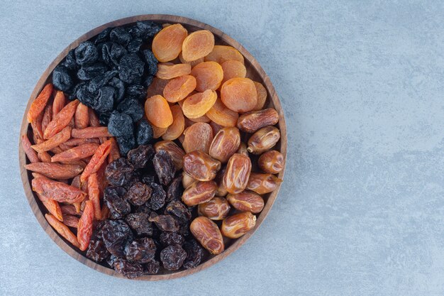 Dried fruits in the wooden board, on the marble table. 