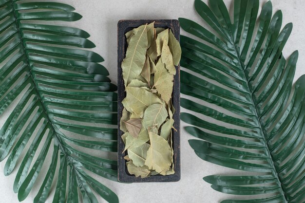 Dried green bay leaves on a wooden plate.