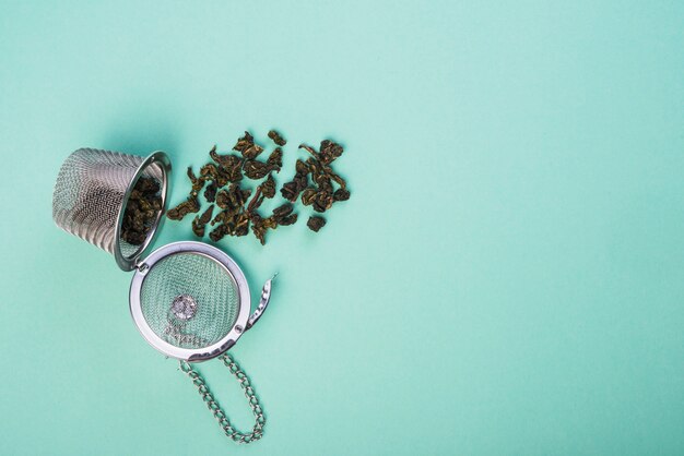 Сушеный травяной чай пролитый из чайного ситечка на синем фоне