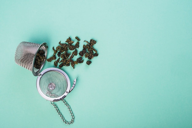 Dried herb tea spilled from the tea strainer on blue backdrop