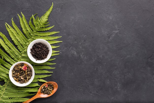 Сушеный травяной чай в белой керамической миске с листьями папоротника на черном фоне