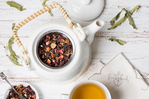 Dried herbs in white teapot with tea on wooden table