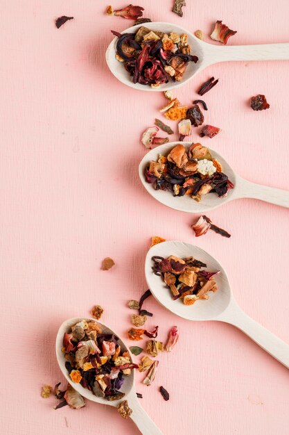 Dried herbs in wooden spoons on a pink.