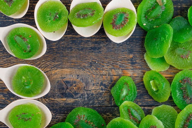 Free photo dried kiwi slices in spoons on wooden background, flat lay.