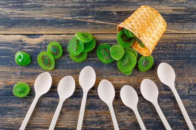 Dried kiwi slices in a wicker basket with spoons flat lay on a wooden background