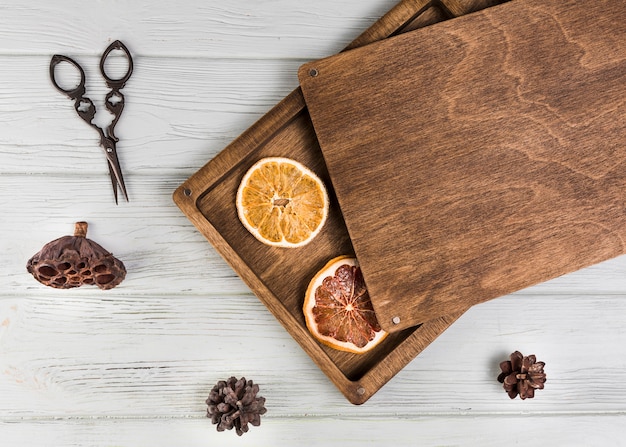 Dried orange; grapefruit slice; lotus pod; pinecone with scissor on white wooden table