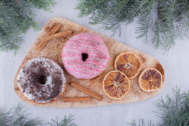 Dried orange slices, donuts and cinnamon sticks on a board on white background.