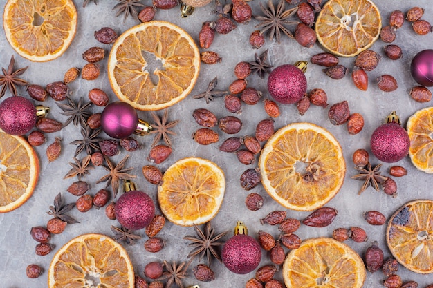 Free photo dried orange with christmas balls and rosehips on stone surface.