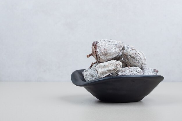 Dried persimmon fruits in black bowl on beige surface