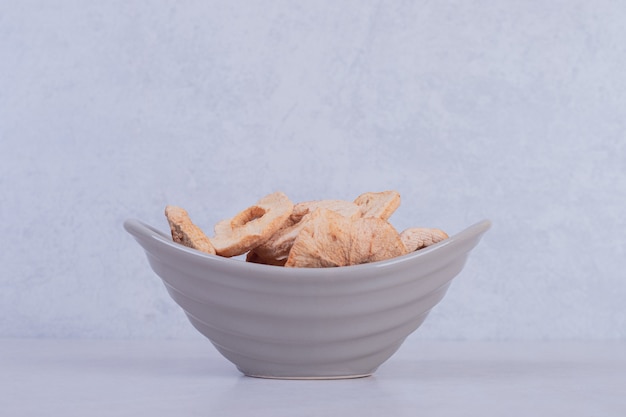 Dried pineapple rings in bowl on white surface.