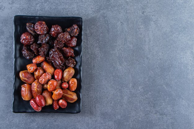 Dried plum and oleaster on a plate, on the marble background.