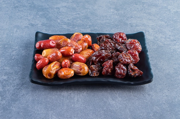 Free photo dried plum and oleaster on a plate, on the marble surface