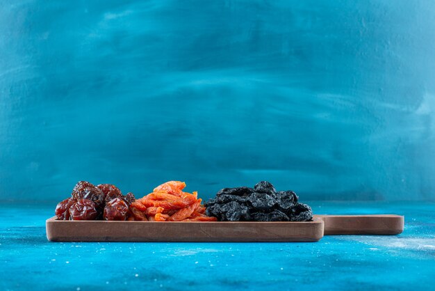 Dried plums and apricots on a board on the blue surface