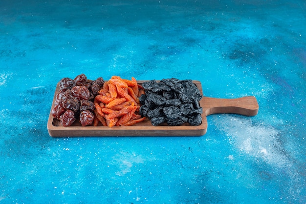 Dried plums and apricots on a board on the blue surface