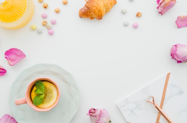 말린 장미; 크로와상; 사탕; 레몬 티; 펜 및 흰색 테이블에 메모장