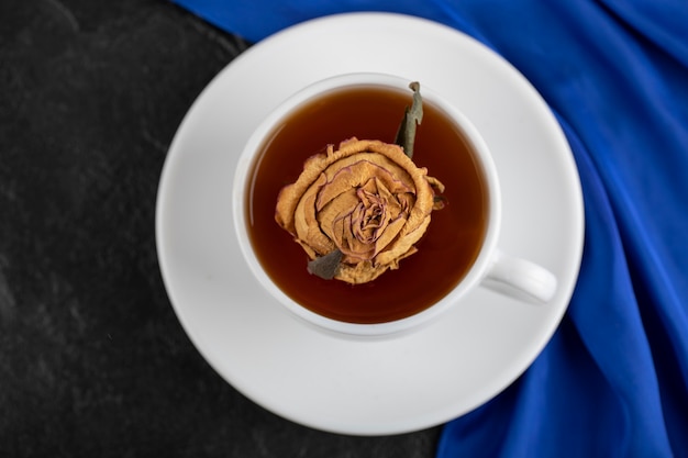 Dried rose in a cup of hot tea on a black table . 