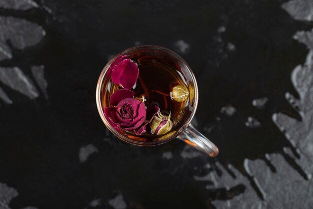 黒いテーブルの上で熱いお茶のカップで乾燥したバラ。