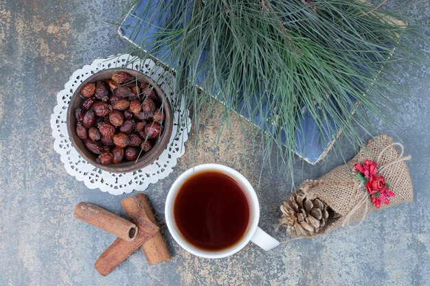 Dried rose hips, cup of tea and cinnamon on marble surface. High quality photo