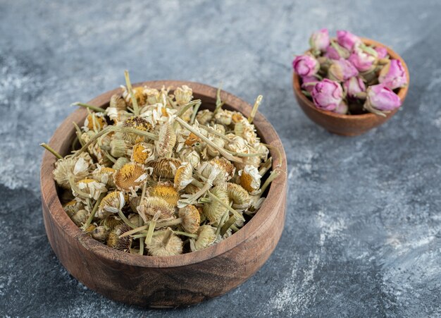 Dried rose petals and chamomiles in wooden bowls. 