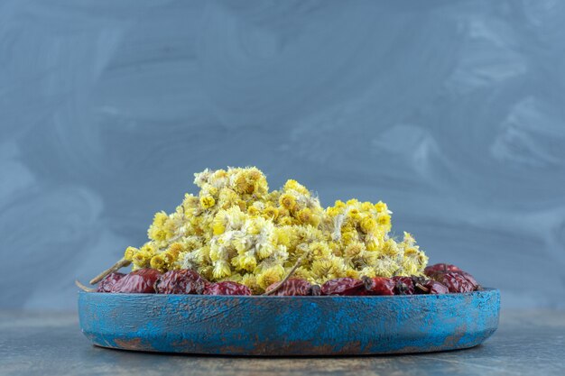 Dried rosehips and flowers on blue plate.