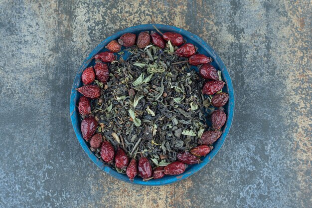 Dried rosehips and tea leaves on blue plate.