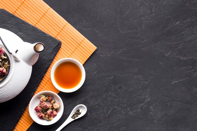 Dried roses and herbal tea in ceramic bowl on black surface