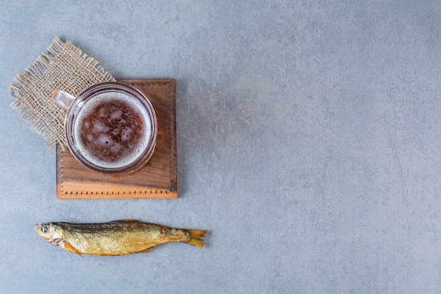 Dried salted fish and beer mug on a board on the marble surface