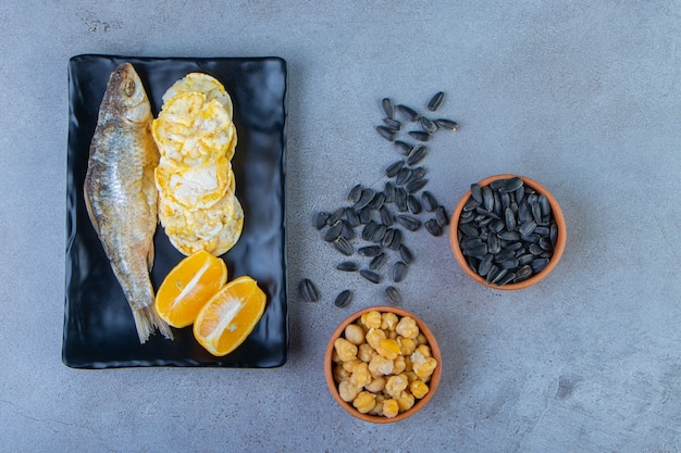대리석 표면에 있는 병아리콩과 씨앗 그릇 옆에 있는 접시에 소금에 절인 생선, 칩, 얇게 썬 레몬. 프리미엄 사진