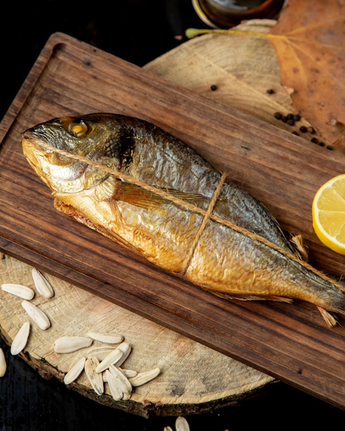 Foto gratuita il pesce affumicato secco avvolto nella corda è servito con il limone mezzo sul bordo di legno