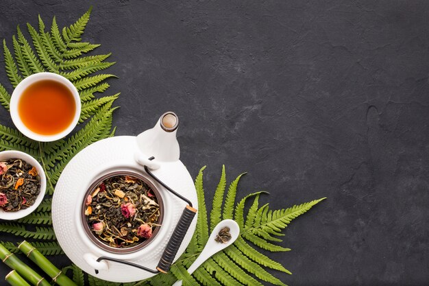 Dried tea herb with fern leaves and bamboo stick over black textured backdrop