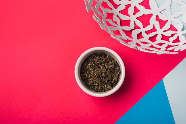 Сушеные листья чая в белой миске на цветном фоне
