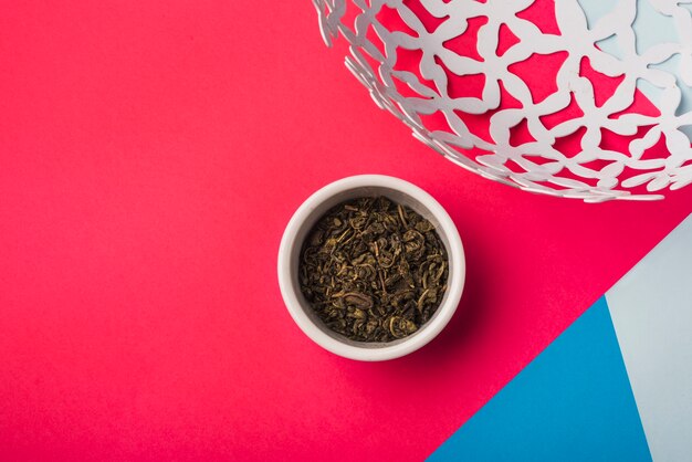 Dried tea leaves in the white bowl against colored backdrop