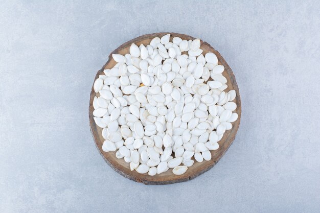 Dried and washed white pumpkin seeds on a log slice on marble background.