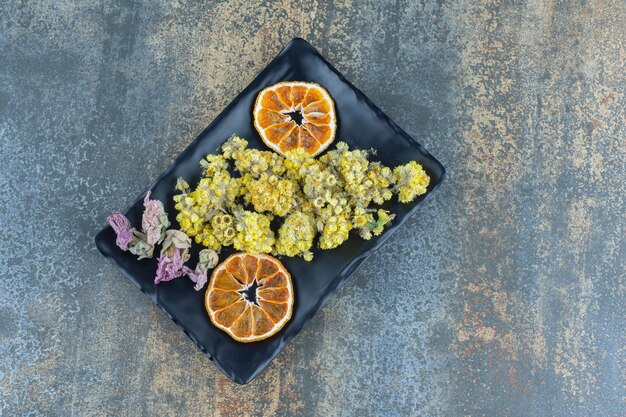 Free photo dried yellow flowers and orange slice on black plate.