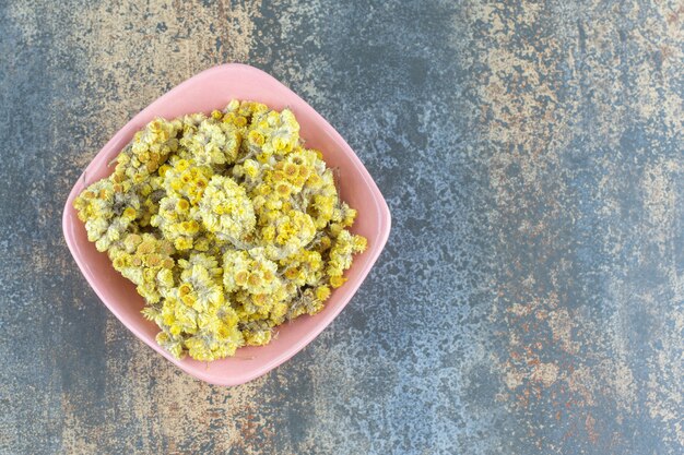 Dried yellow flowers in pink bowl.