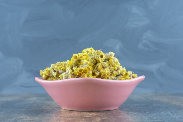 Dried yellow flowers in pink bowl.