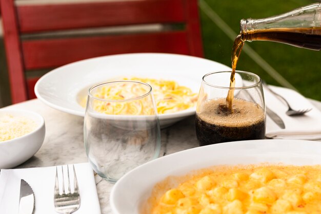 Drink pouring into the glass with tasty italian pasta food on table at restaurant