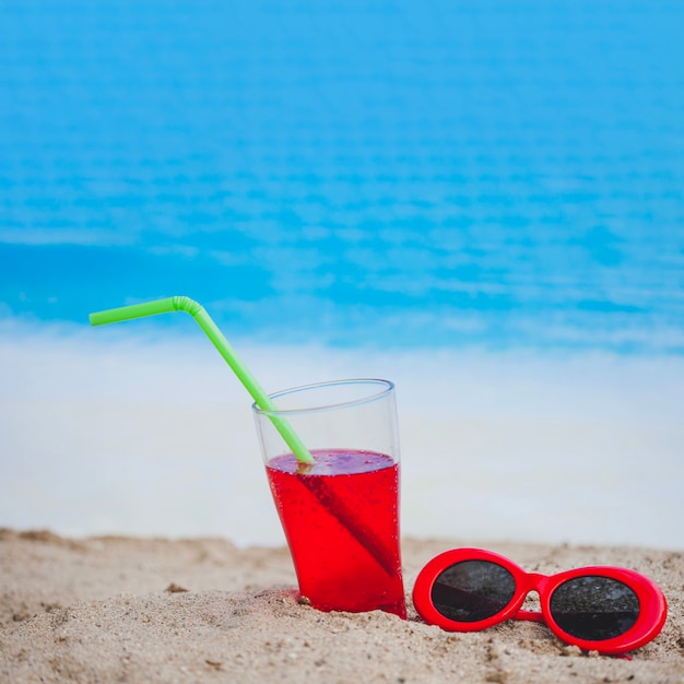 Drink and red sunglasses on sandy surface