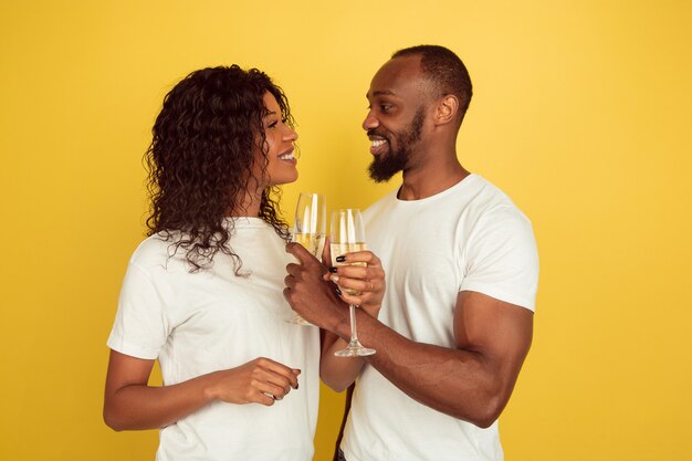 Drinking champagne. Valentine's day celebration, happy african-american couple isolated on yellow studio background. Concept of human emotions, facial expression, love, relations, romantic holidays.