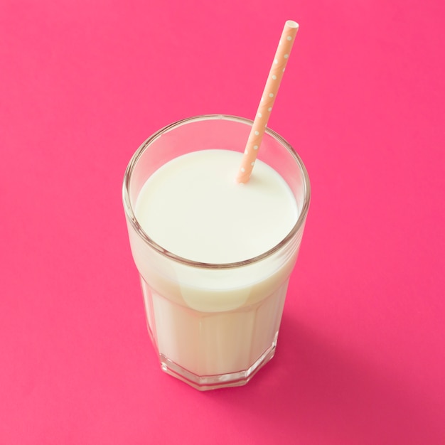Питьевая солома в стакане молока на розовом фоне