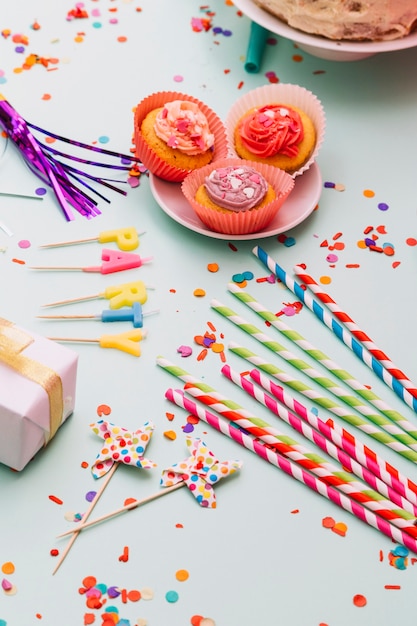 Drinking straws; prop; candles; cupcake; gift box; and confetti on blue background