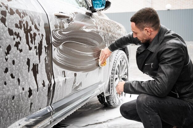 Driver washing his car by sponge with soap solution