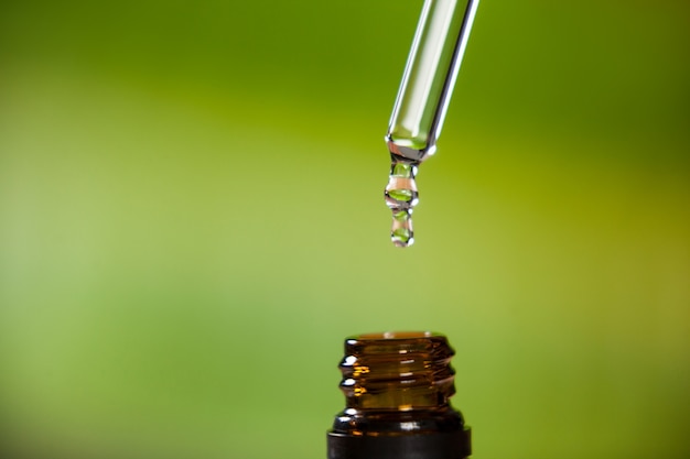 Drop of oil dripping from pipette into bottle of essential oil