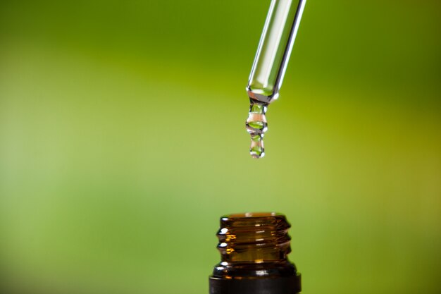 Drop of oil dripping from pipette into bottle of essential oil