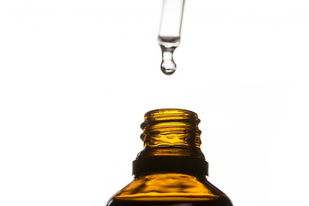 Drop of oil dripping from pipette into bottle of essential oil