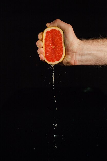 Drops of grapefruit juice fall from fruit on black background