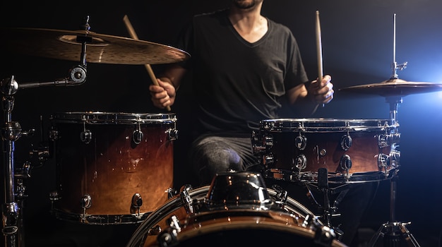 The drummer plays drums while sitting at the drum kit on stage