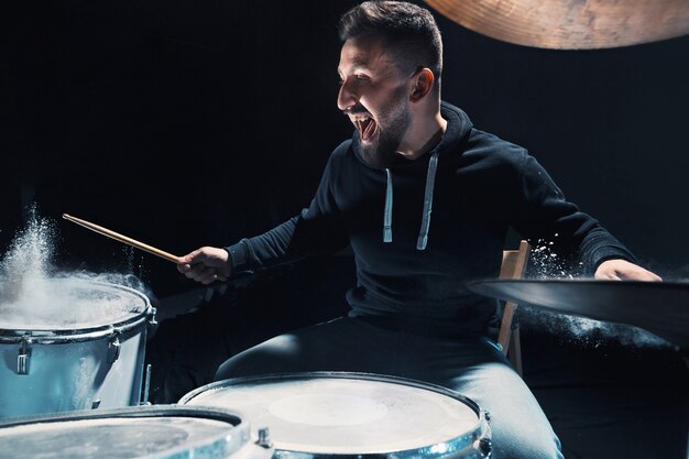 Drummer rehearsing on drums before rock concert. Man recording music on drum set with show effect in the form of flour