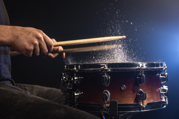 Drummer using drum sticks hitting snare drum with splashing water on black background under studio lighting close up.