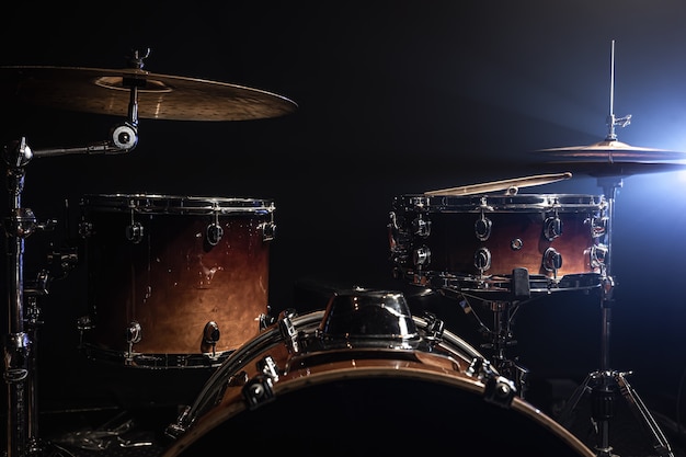 Drums, bass drum, hi-hat, cymbals on a dark background with beams from a spotlight, copy space.